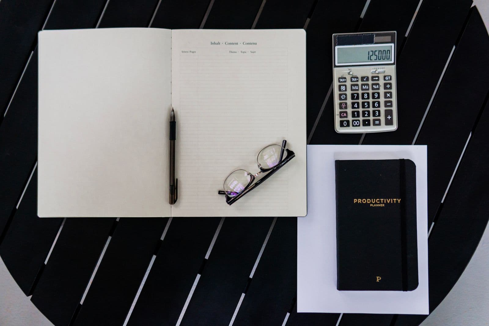 A notebook, calculator and productivity planner laid out on a black table