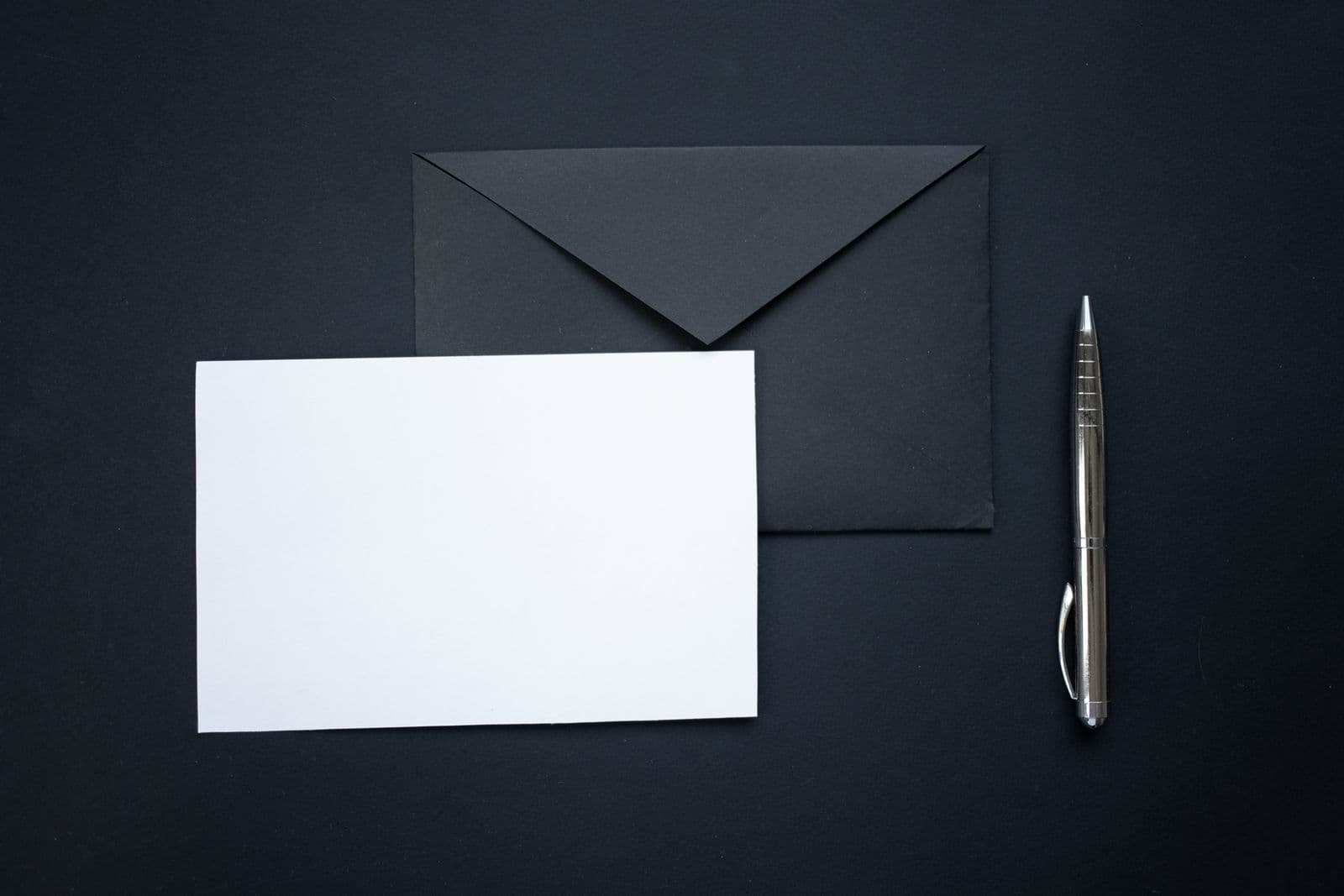 Black envelope, a blank white card and a silver pen on a black surface