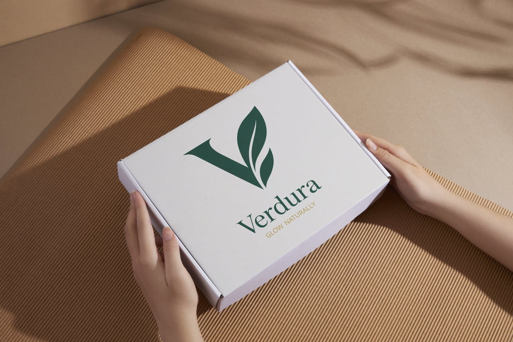 Hands holding a white Verdura shipping carton printed with the green leaf monogram